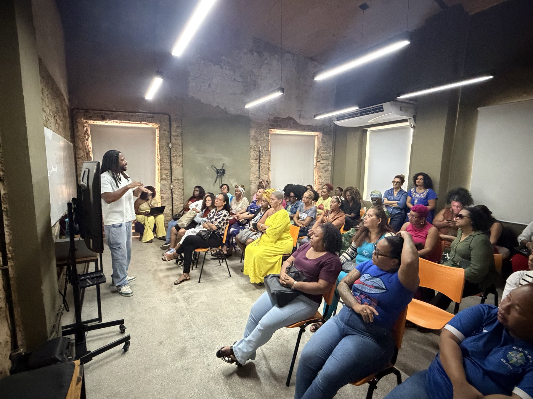 denison luz falando em pé para uma sala cheia na fábrica cultural, em salvador, com o público sentado acompanhando